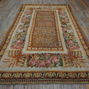 Ornate tan and rust rug featuring dense pink roses rests on distressed wood planks.
