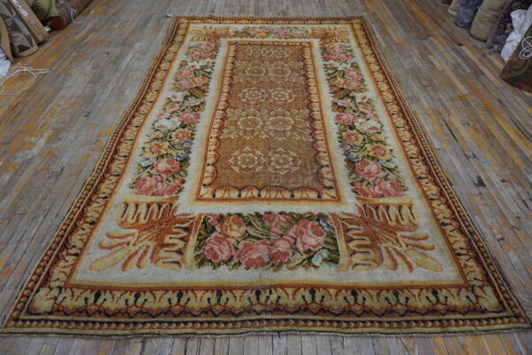 Ornate tan and rust rug featuring dense pink roses rests on distressed wood planks.