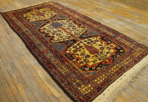 Geometric tribal rug in red, yellow, black, and blue patterns rests diagonally on rustic hardwood flooring.