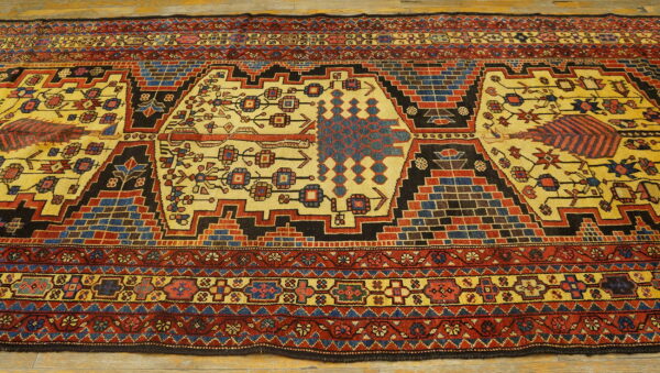 Yellow-gold rug with geometric medallion and border patterns in red, blue, and black rests on wood flooring.