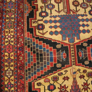 Geometric rug detail showing tan, red, blue, and black patterns, including stepped motifs, resting on wood.