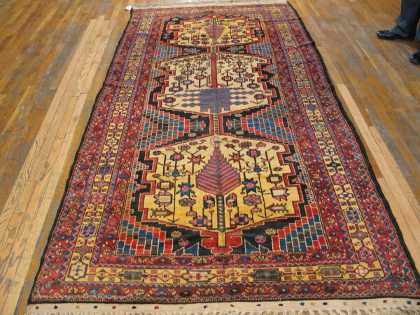 Low-pile, tribal rug featuring red, yellow, blue, and black geometric patterns on a wood floor.
