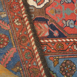 Close-up of a low-pile rug showing intricate red, blue, and brown geometric patterns on wood flooring.