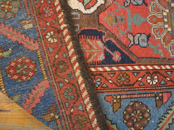 Close-up of a low-pile rug showing intricate red, blue, and brown geometric patterns on wood flooring.