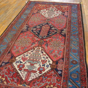 Low pile runner rug with geometric red field and multi-banded blue borders on a light wood floor.