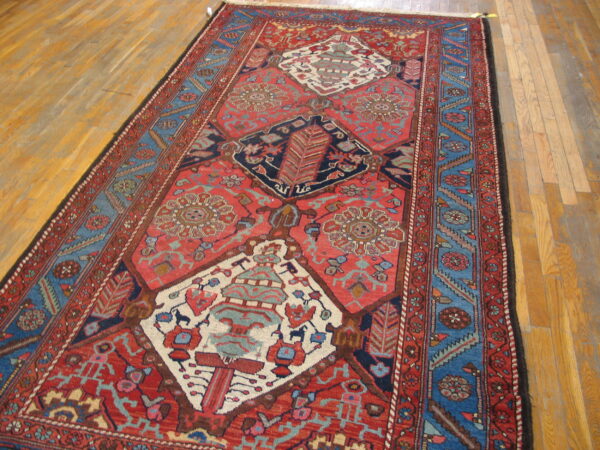 Low pile runner rug with geometric red field and multi-banded blue borders on a light wood floor.