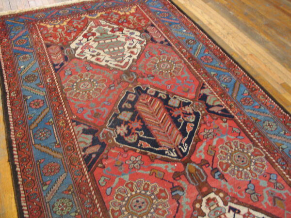 Red and blue traditional rug featuring medallions and geometric borders on light brown hardwood floors.