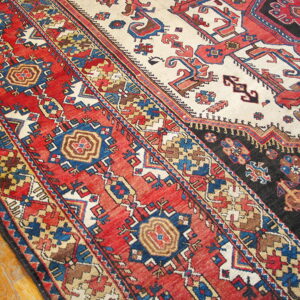 Geometric pattern rug featuring red borders, a cream field, and black accents rests on hardwood floors.