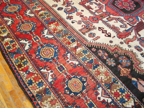 Geometric pattern rug featuring red borders, a cream field, and black accents rests on hardwood floors.