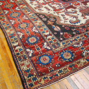 Corner of a low-pile rug with geometric red, blue, and cream patterns resting on a golden wood floor.