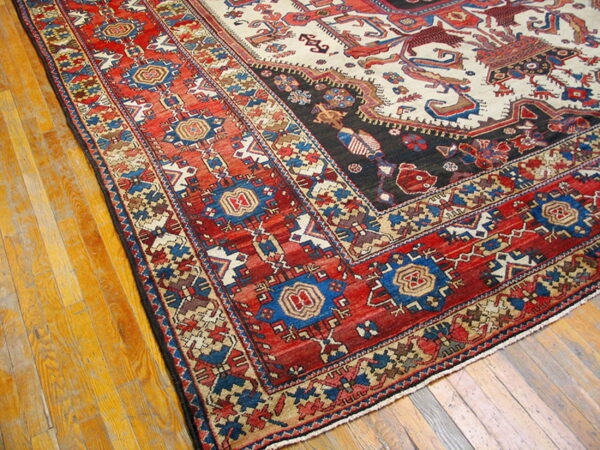 Corner of a low-pile rug with geometric red, blue, and cream patterns resting on a golden wood floor.