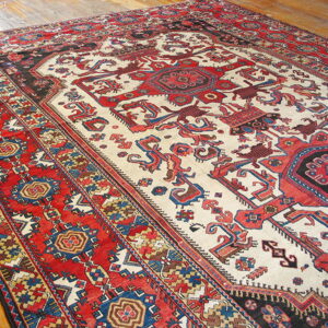 Red and off-white tribal rug with geometric patterns and blue accents rests on wood planks.