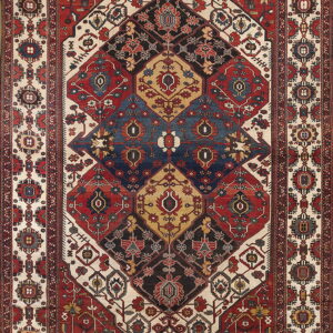 Intricate low-pile rug featuring a large central geometric pattern in red, blue, cream, and black.