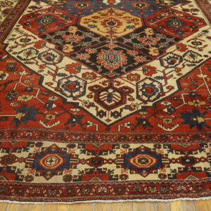 Geometric red and cream rug featuring a prominent dark central medallion laid over wood planks.