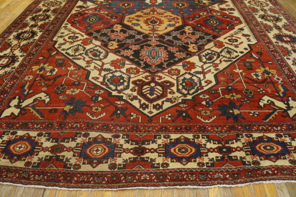 Geometric red and cream rug featuring a prominent dark central medallion laid over wood planks.