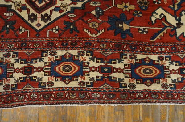 Red and cream textured rug with geometric blue patterns displayed on rustic wood planks.