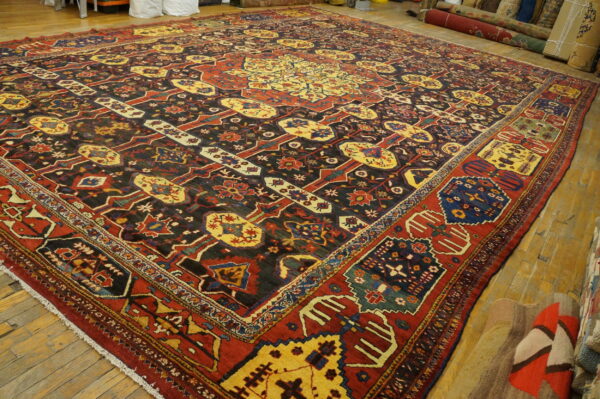 Ornate traditional rug in red, yellow, and dark blue patterns covers worn light brown hardwood flooring.