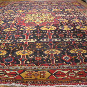 Giant traditional rug with a detailed red, gold, and dark blue repeating pattern displayed on wood flooring.