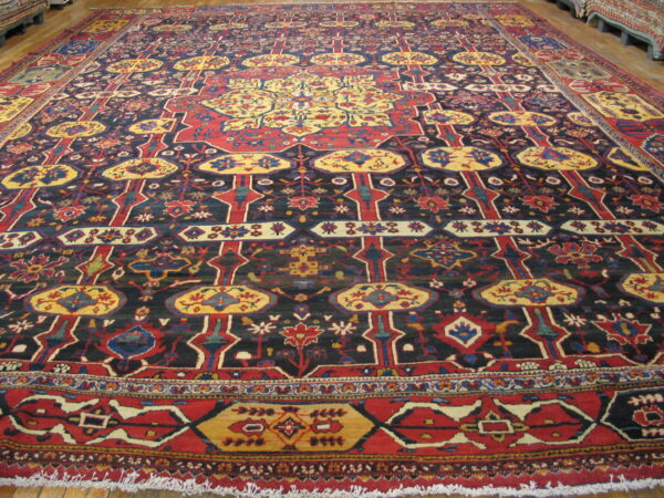 Giant traditional rug with a detailed red, gold, and dark blue repeating pattern displayed on wood flooring.