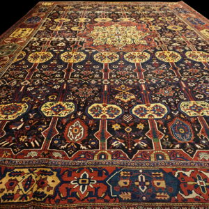 Dark area rug featuring complex traditional patterns in navy, red, and gold, angled on a black background.
