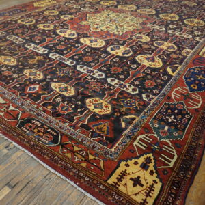 Geometric patterned area rug in dark blue, red, and gold, laid on worn light brown plank flooring.