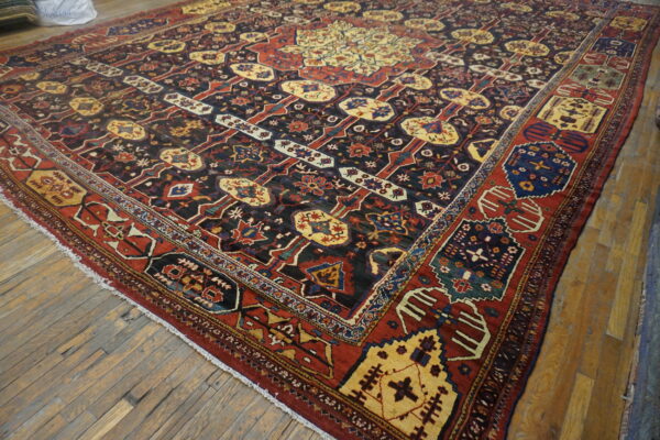 Geometric patterned area rug in dark blue, red, and gold, laid on worn light brown plank flooring.