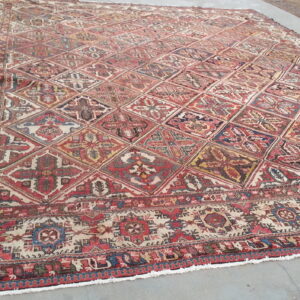 Large, low-pile rug with a red, blue, and yellow geometric diamond lattice pattern rests on gray concrete.