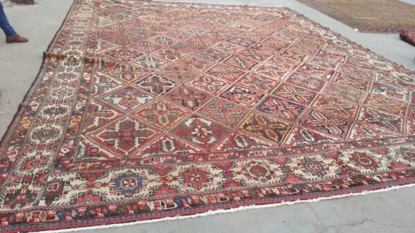 Large, low-pile rug with a red, blue, and yellow geometric diamond lattice pattern rests on gray concrete.