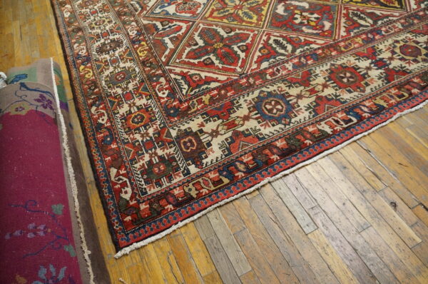 Low-pile red, cream, and blue geometric rug corner on rustic hardwood floors with rolled rugs nearby.