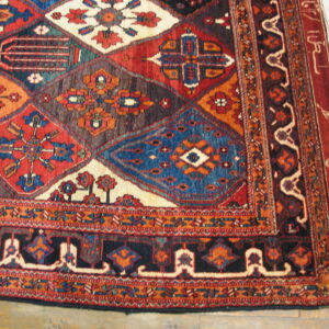 Geometric rug corner featuring diamonds and elaborate borders in red, blue, black, and ivory on wood.