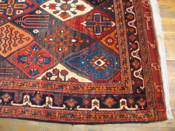 Geometric rug corner featuring diamonds and elaborate borders in red, blue, black, and ivory on wood.
