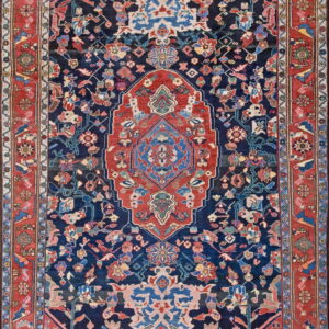 Detailed, low-pile rug with a red and blue medallion centering a dark navy field and a contrasting red border.