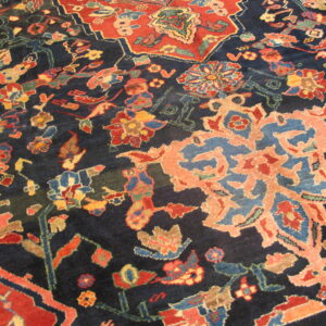 Intricate traditional rug pattern featuring coral, red, and blue floral motifs on a deep navy background.