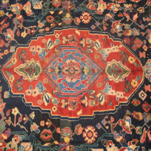 Navy blue and rust red rug featuring a prominent central medallion and dense multicolored floral patterns.