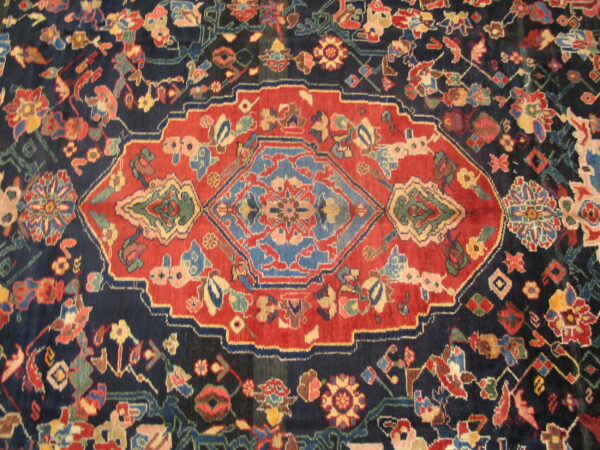 Navy blue and rust red rug featuring a prominent central medallion and dense multicolored floral patterns.