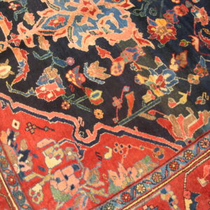 Detailed low-pile rug showing a complex coral and blue floral pattern on a navy field and a red border.