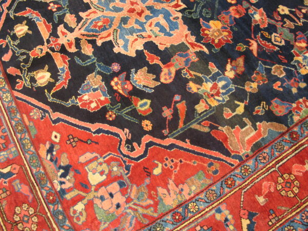 Detailed low-pile rug showing a complex coral and blue floral pattern on a navy field and a red border.