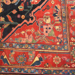A corner detail of a deep red and navy rug with highly stylized, colorful traditional motifs and multiple borders.