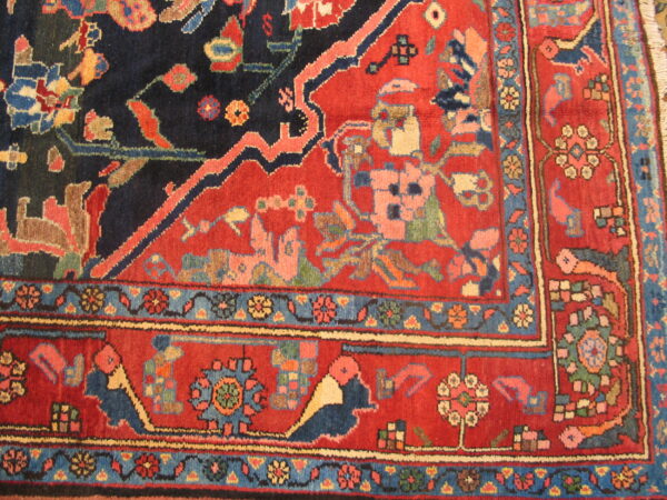 A corner detail of a deep red and navy rug with highly stylized, colorful traditional motifs and multiple borders.