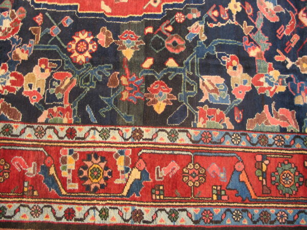 Detail view of a rug showing a navy field and red border filled with complex, colorful geometric figures.