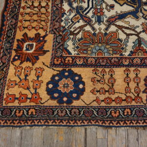 Geometric rug corner featuring tan, rust, and blue medallions resting on weathered gray wood flooring.
