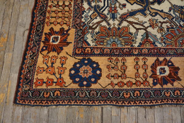 Geometric rug corner featuring tan, rust, and blue medallions resting on weathered gray wood flooring.