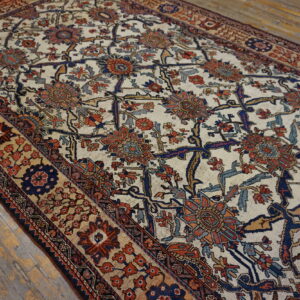 A traditional rug with an ivory field, featuring navy, rust, and blue floral motifs, laid on distressed wood floorboards.