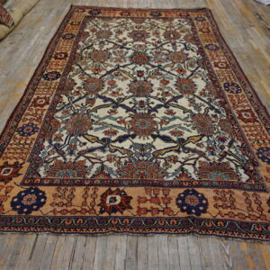 Ornate cream rug with blue, red, and tan botanical patterns on a distressed wooden floor.