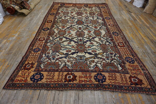 Ornate cream rug with blue, red, and tan botanical patterns on a distressed wooden floor.