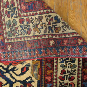 Geometric red, blue, and cream rug corner folded to show the backing and fringe on wood planks.