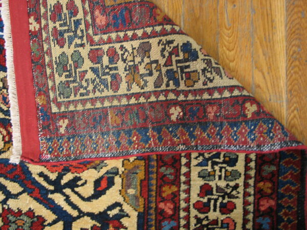 Geometric red, blue, and cream rug corner folded to show the backing and fringe on wood planks.