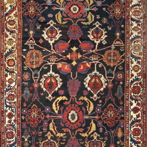 Dark navy rug with a dense traditional pattern of red, blue, and gold florals, framed by a wide ivory border.