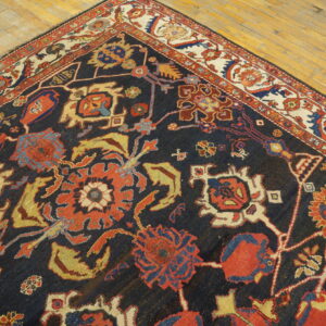 Low-pile rug with navy field, complex red and yellow motifs, and cream border resting on wood planks.