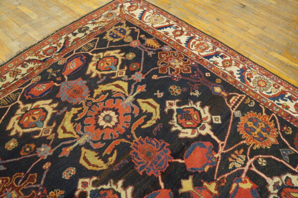 Low-pile rug with navy field, complex red and yellow motifs, and cream border resting on wood planks.